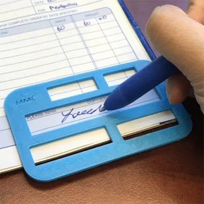 A bright blue plastic signature guide — a flat rectangular frame with a long open window across its middle — laid over a paper check register, while a hand signs in ink inside the window with a blue pen, the frame's raised edges keeping the signature level and inside the line.
